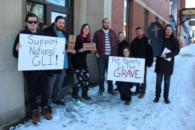 A group of people hold up a mock coffin and signs encouraging a guaranteed livable income