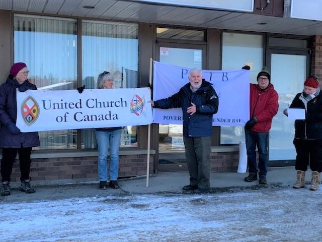 Several people hold up a United Church of Canada banner and signs supporting a guaranteed livable income.