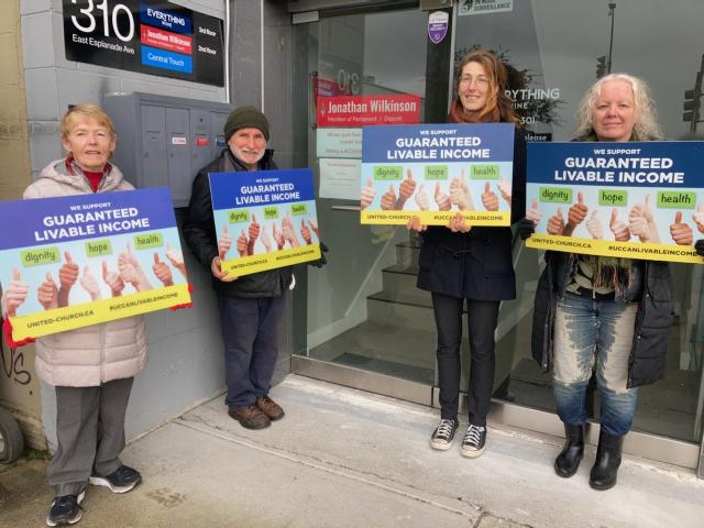 Four people hold signs urging a guaranteed livable income