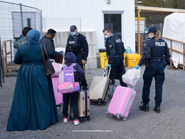 RCMP officers help a family of three asylum seekers, including a child, with their luggage at Roxham Road.
