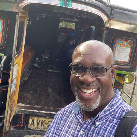 Rev. Dr. Japhet Ndhlovu, smiling, takes a selfie with a jeepney in the background.