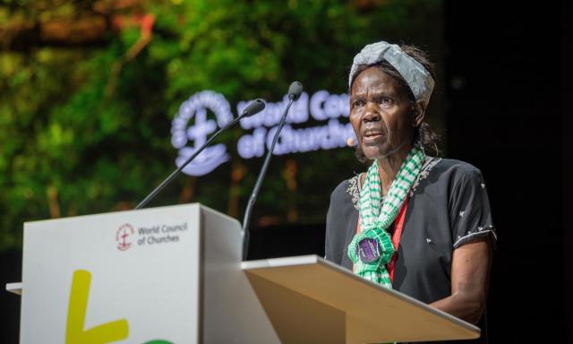 Agnes Abuom stands at a lectern with the World Council of Churches name and logo behind her.