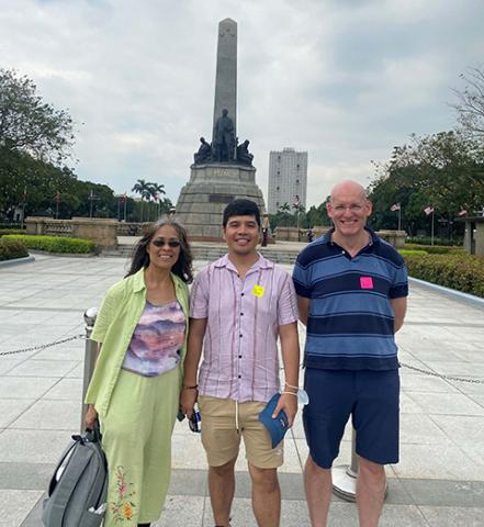 A woman and two men stand in front of a large statue in a park