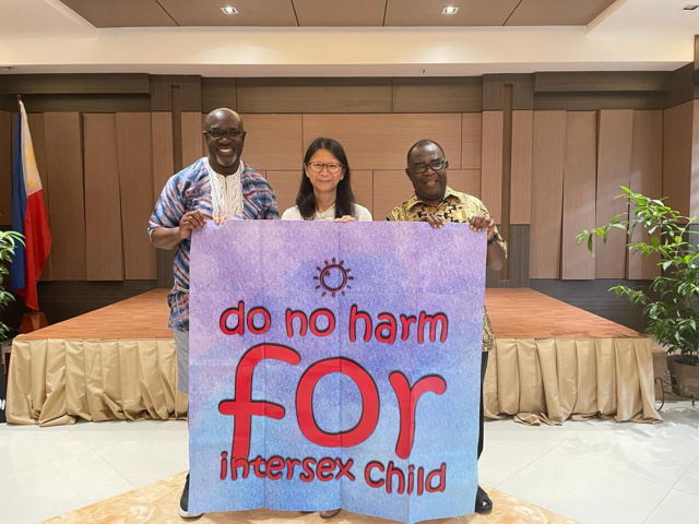 Three participants in the consultation hold a large pink sign saying "Do No Harm for Intersex Child"