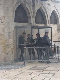 A Palestinian teenager is questioned by three soldiers at a checkpoint in a stone wall.