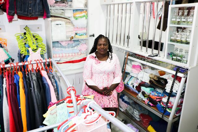 A woman sits smiling in her clothing store surrounded by racks of clothes