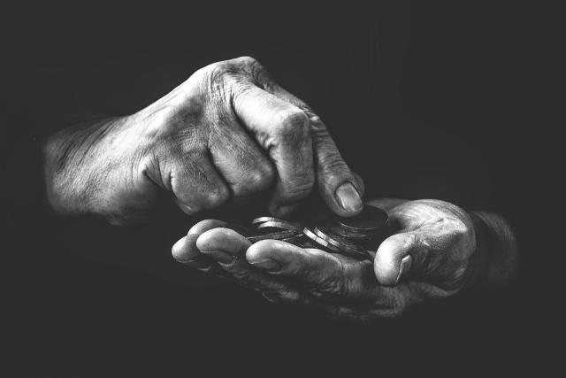 In a shadowy, black and white photo, hands pick up coins.