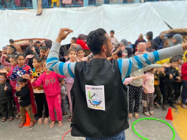 A young man leads a large group of children in a game.