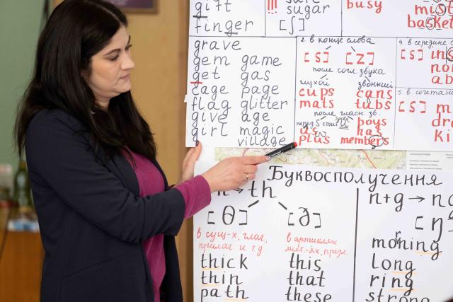 A woman points at a whiteboard covered in English and Ukrainian words.