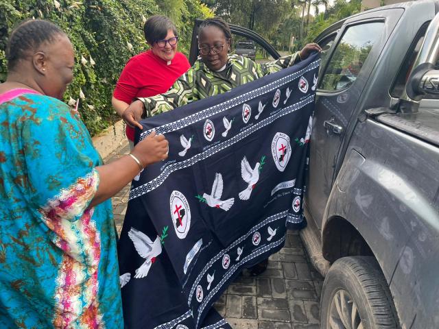 Dr. Emily Sikazwe and Dr. Mwiche Zulu wrap the Moderator in a beautiful black cloth printed with white doves.