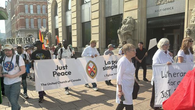 People holding a United Church banner and signs calling for peace march along an Ottawa street.