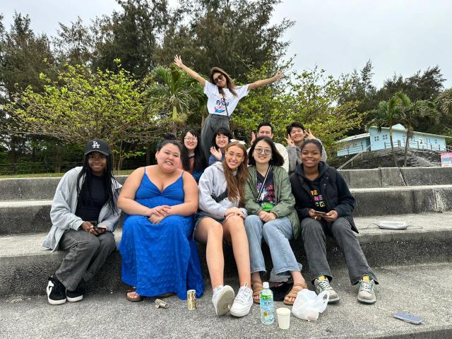 Eleven young people sit on steps smiling and waving at the camera