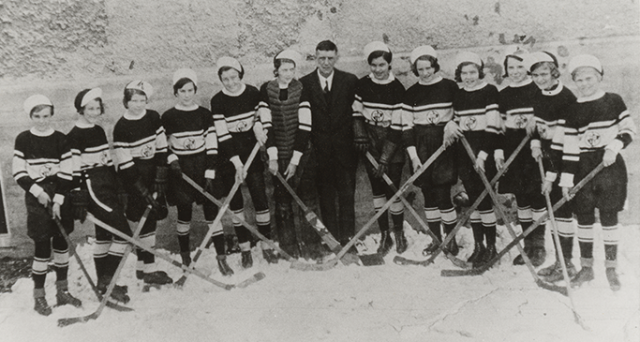 A black and white photo of a team of young women hockey players with their coach