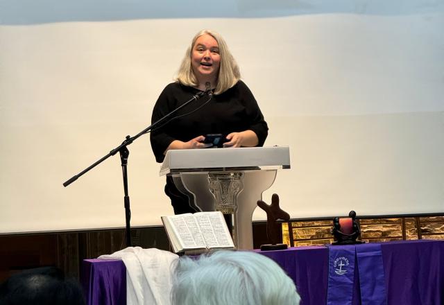Emily Dwyer speaks at a podium that has an open Bible and cross in front of it.