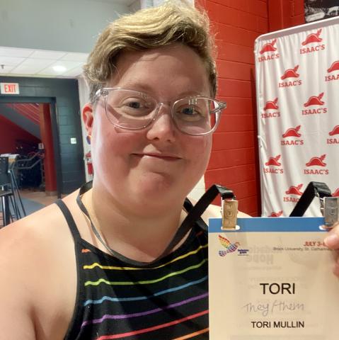 Author Tori Mullin (pronouns they/them) holds up a attendee badge for the event.