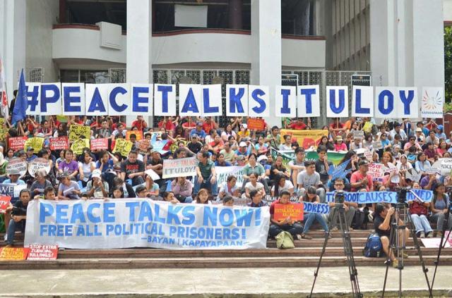 Large group of people hold up banners and signs urging peace talks in the Philippines.