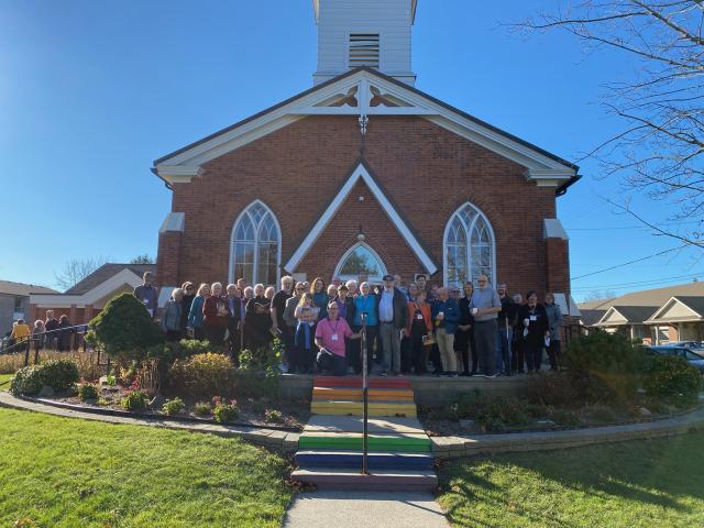 40 people in front of a church door with rainbow-painted steps.