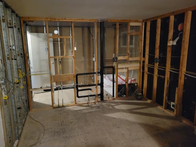 The interior of a house, stripped to the frames, with plumbing and electrical wires revealed.