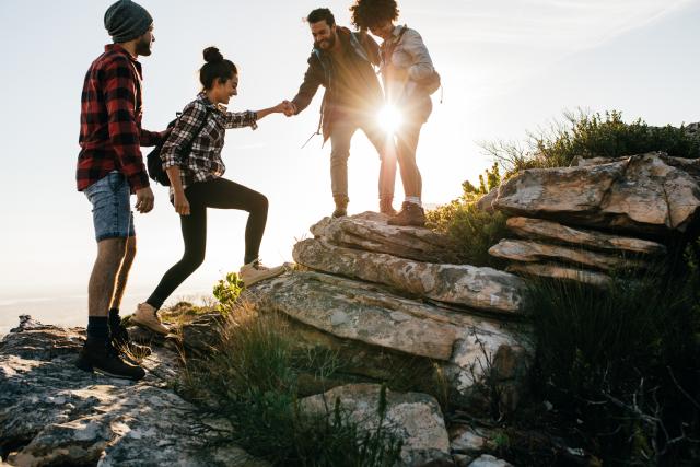 Several people help each other climb a steep hill 