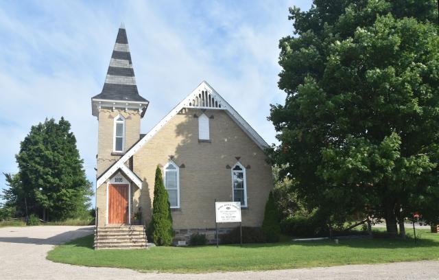 A small white church with a steeple, between two trees.