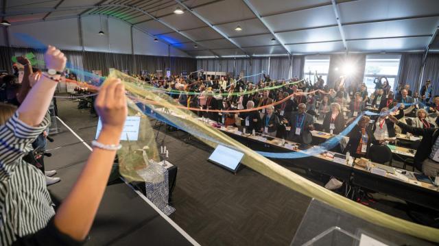 A large room full of people holding ribbons together that reach across the room.