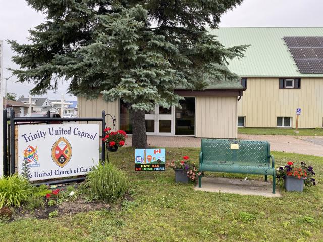A small church with a large pine tree in the foreground and a sign reading "Trinity United Church Capreol"