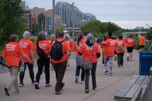 A group of people walking along a pathway wearing orange shirts.