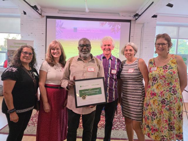 Six people in front of a colourful background, one of which is holding a framed certificate.