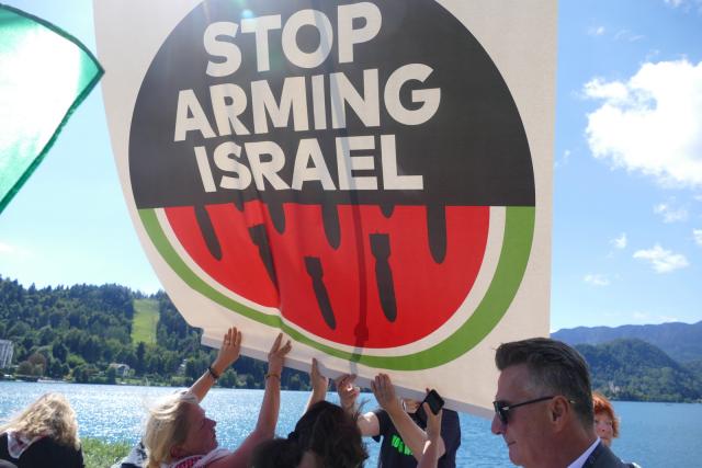 A small group of people holding up a sign that reads "Stop Arming Israel"