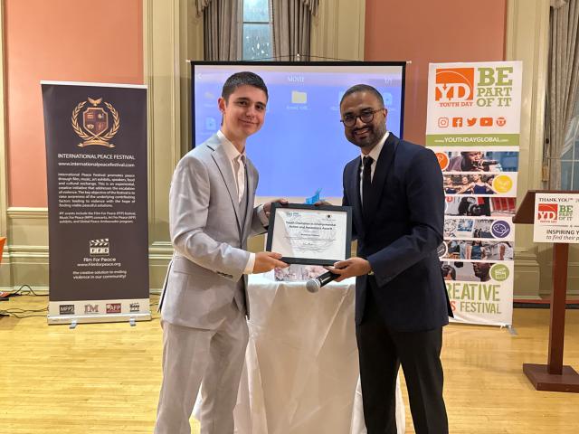 A young man in a suit receives a plaque from another man in a suit at an awards ceremony.