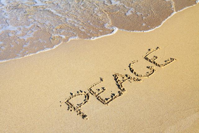 The word "Peace" written in sand on a beach with the shore partially visible.