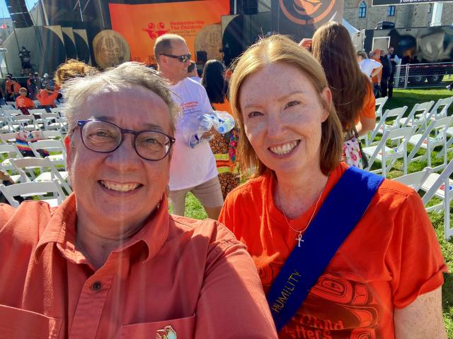 Two women taking a selfie wearing orange shirts standing on a field.