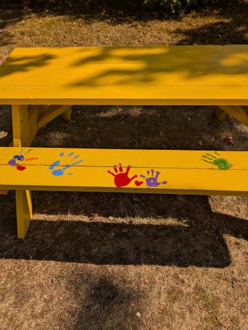 A yellow picnic table with painted handprints on it 