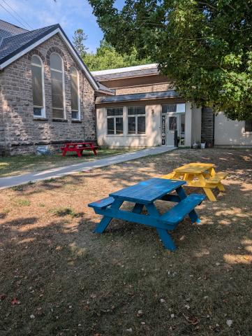 Picnic tables sitting outside of a church in the shade on a sunny day
