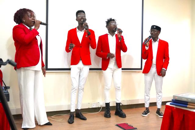 Four people in red jackets and white pants with microphones leading a worship service