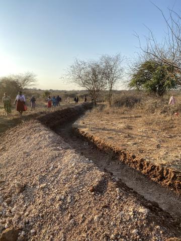 A group of people walk past a large trench dug in dirt