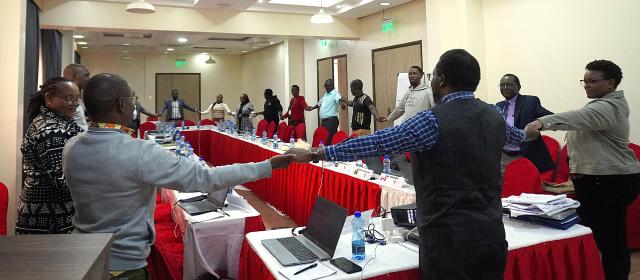 A group of people holding hands standing around a conference table