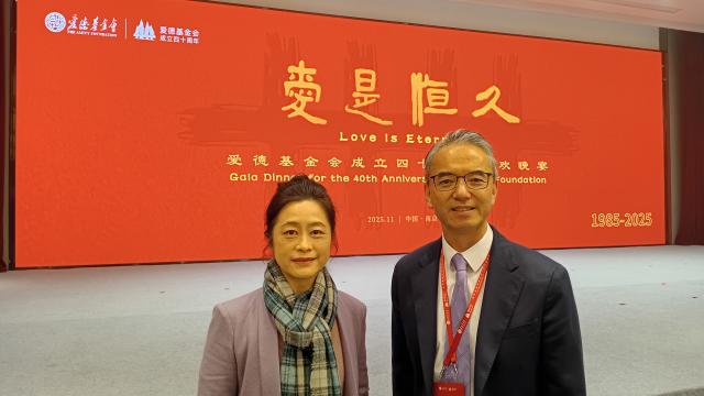 A photo of a man and a woman in front of a red backdrop with yellow Chinese and English phrases written on it
