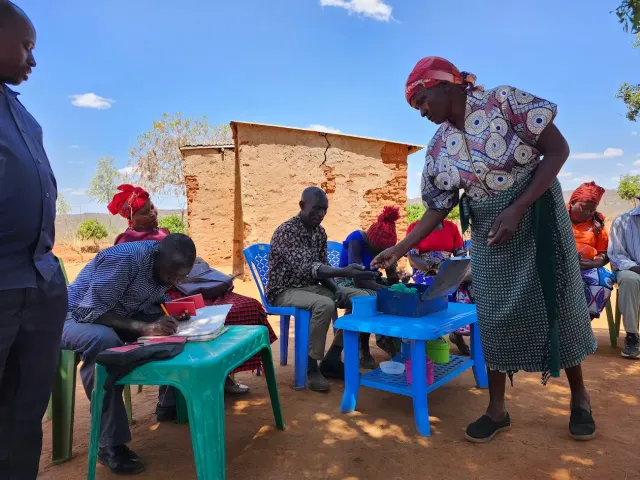 A group of people sitting on plastic chairs and tables outdoors in Kenya