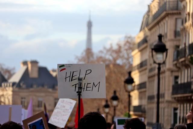 A sign with the words "Help them" is held up at a street protest