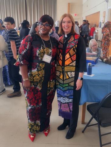 An African woman and white woman in clerical dress smile for a photo
