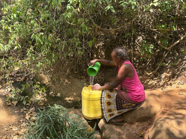 A woman fetching water from a spring with a large plastic jug