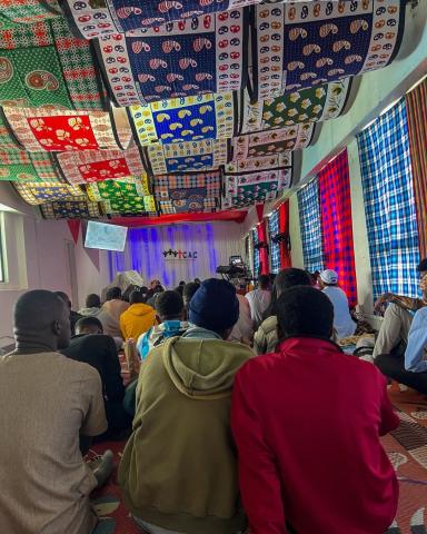 A group of people sit on the floor, with colourful banners overhead