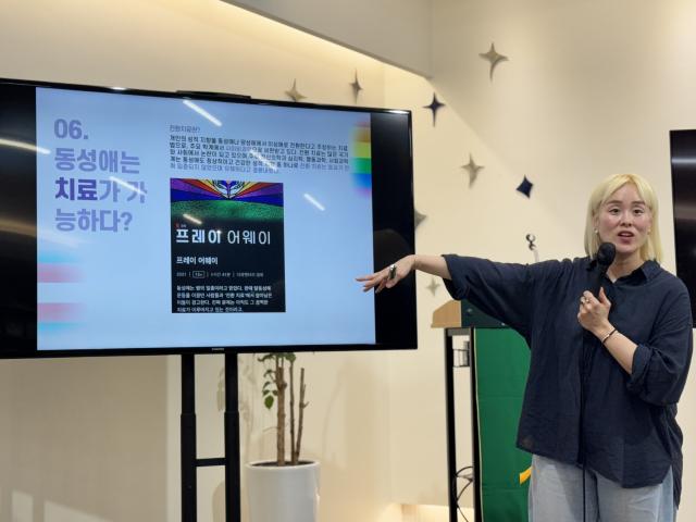 A Korean woman points at a screen with an educational slide on it