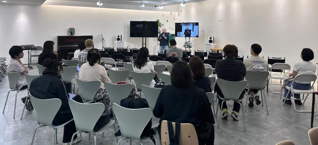 A group of people sit in chairs as a session is taught in a classroom