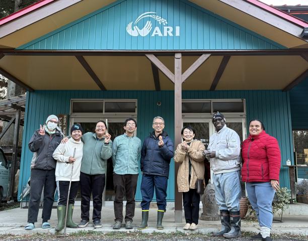 A group of people smiling and holding eggs outside of a farmhouse