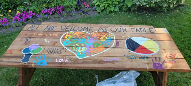 A picnic table with the message "All are welcome at our table" written on it