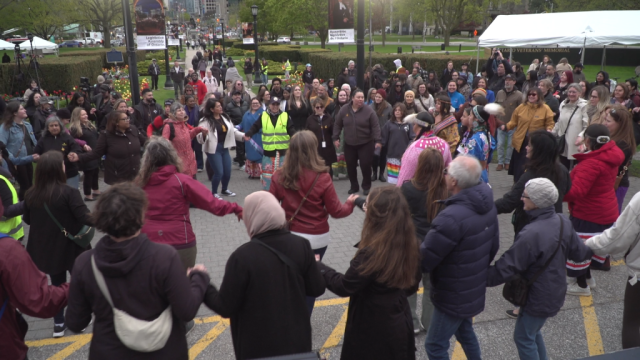 A large group of people dance in a circle on a lawn