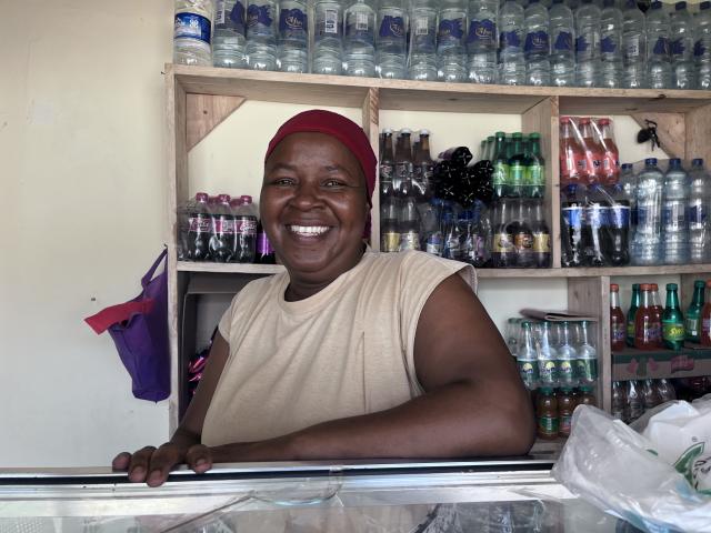 A smiling African woman stands in front of a shelf filled with products