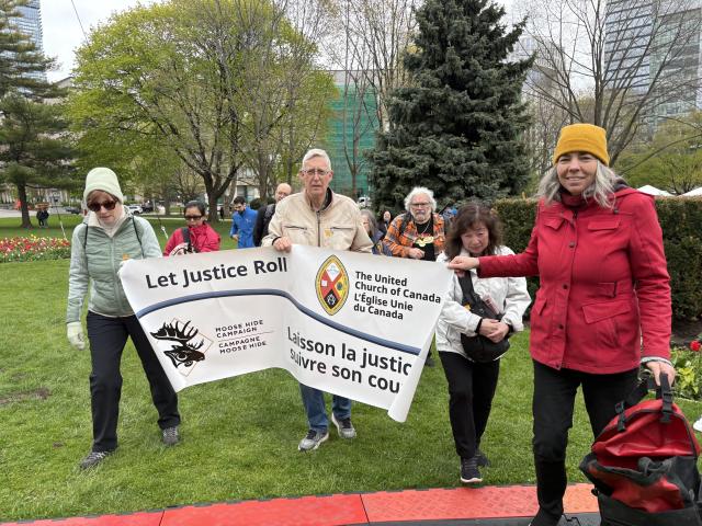 A group of people hold up a banner that reads "Let Justice Roll - The United Church of Canada - Moose Hide Campaign"